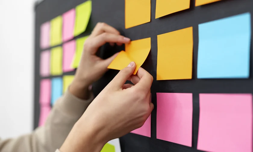 Mãos colocando post-its coloridos em uma parede preta